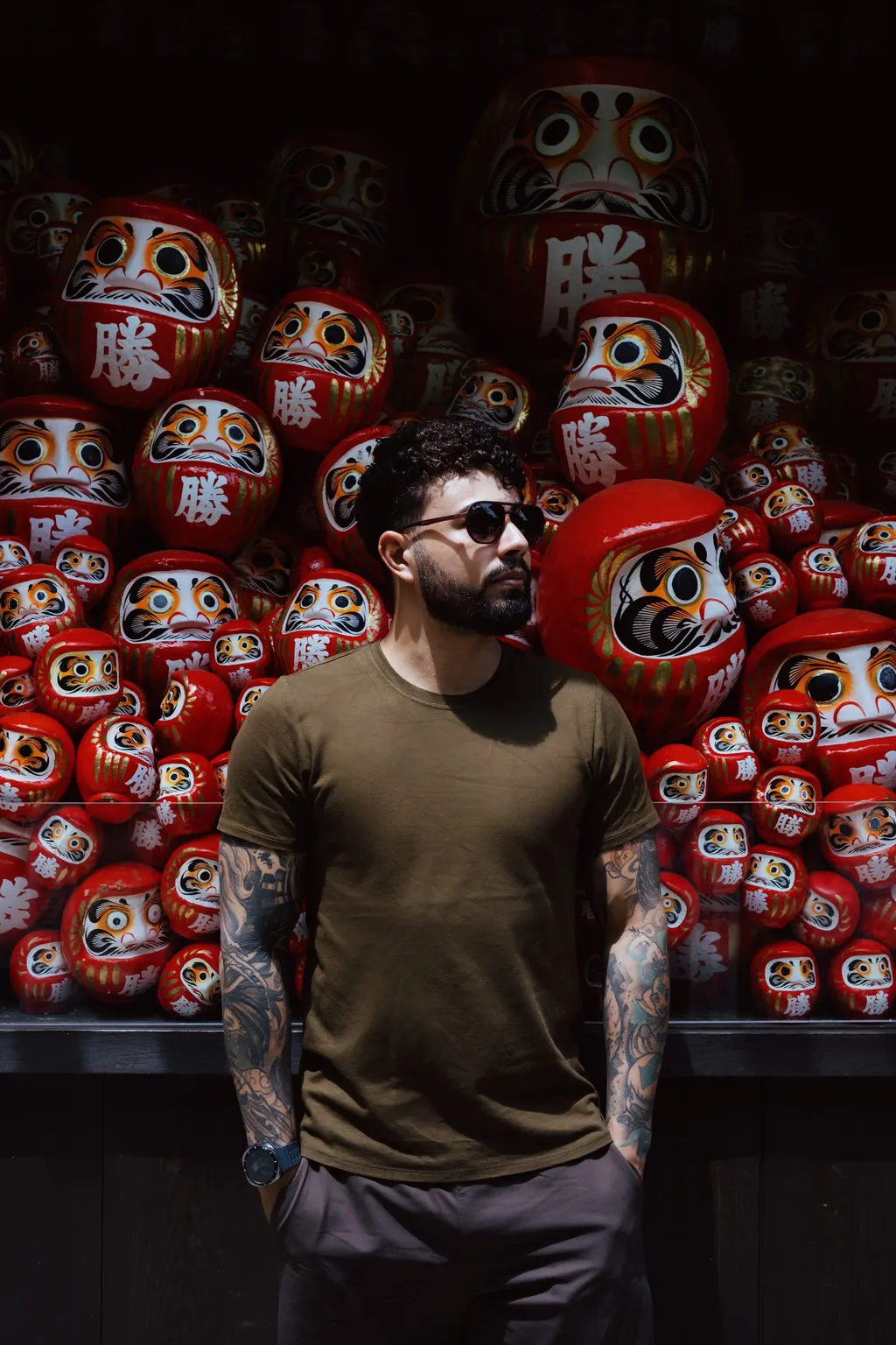 Portrait of Christofer Ramos in front of a wall of daruma at Katsuo-ji, Japan